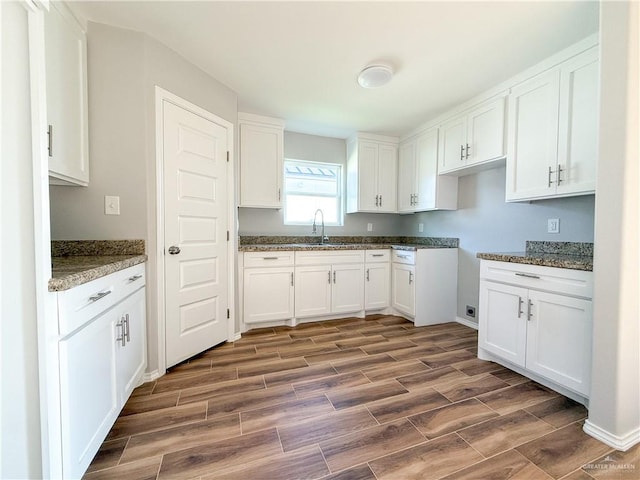 kitchen with dark hardwood / wood-style flooring, white cabinetry, sink, and dark stone counters