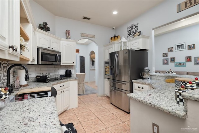 kitchen featuring arched walkways, light tile patterned flooring, stainless steel appliances, visible vents, and decorative backsplash