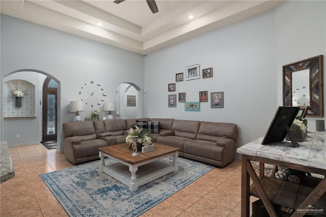 living room featuring light tile patterned floors, arched walkways, ceiling fan, a high ceiling, and a tray ceiling