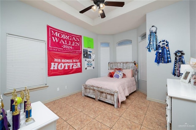 bedroom featuring a ceiling fan, a tray ceiling, light tile patterned flooring, and baseboards