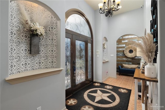 tiled foyer entrance featuring arched walkways, french doors, a high ceiling, a chandelier, and baseboards