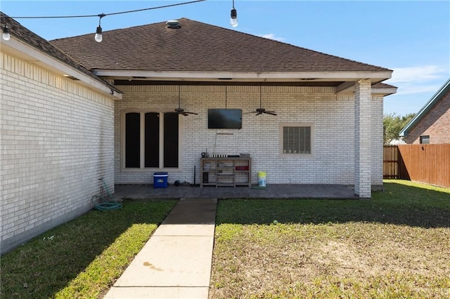 back of house with a ceiling fan, a lawn, roof with shingles, fence, and brick siding