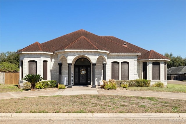 french provincial home with a shingled roof, brick siding, fence, and a front lawn