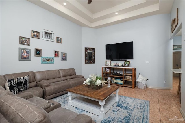 tiled living area featuring baseboards, a tray ceiling, and a ceiling fan