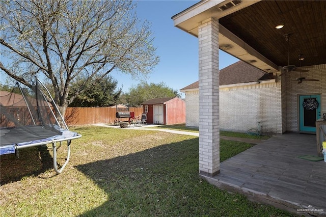 view of yard with a trampoline, an outbuilding, a ceiling fan, a shed, and fence private yard