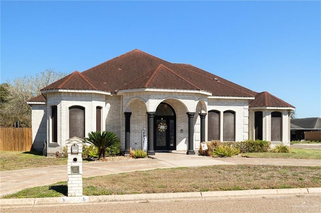 french country home with brick siding, fence, and roof with shingles