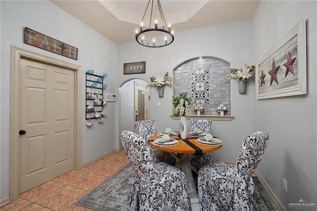 tiled dining area with an inviting chandelier, baseboards, arched walkways, and a raised ceiling