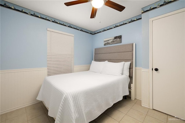 bedroom featuring a wainscoted wall, light tile patterned floors, and a ceiling fan