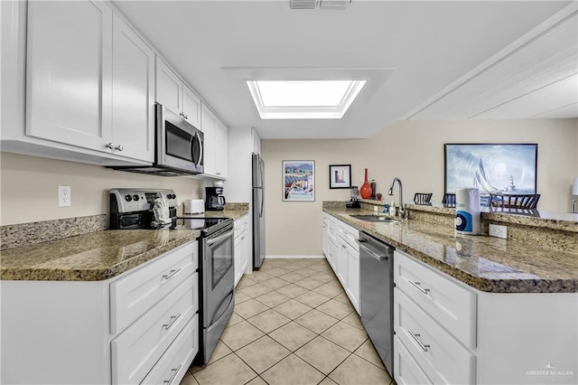 kitchen with a skylight, sink, stainless steel appliances, kitchen peninsula, and white cabinets