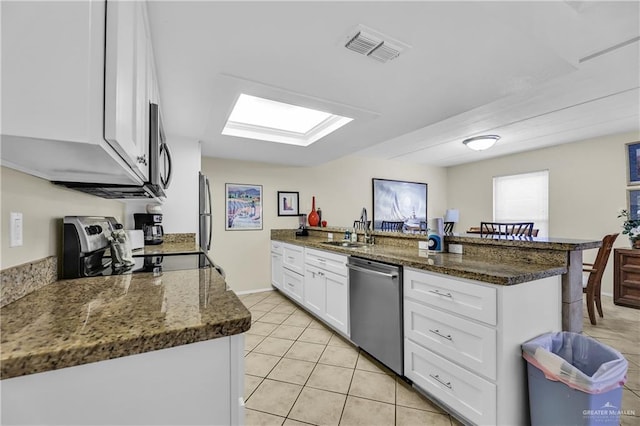 kitchen with white cabinets, sink, light tile patterned floors, kitchen peninsula, and stainless steel appliances