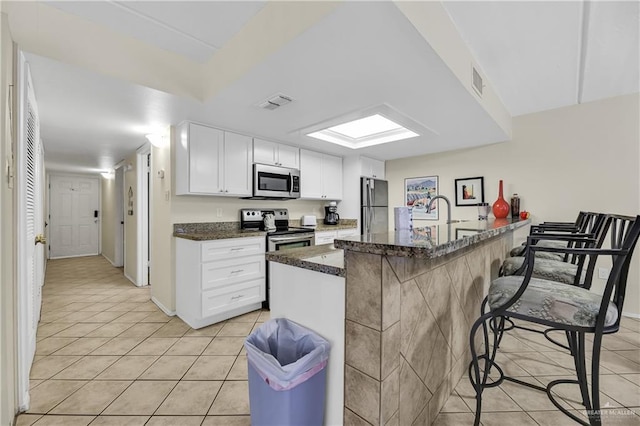 kitchen with light tile patterned floors, white cabinetry, a breakfast bar area, and appliances with stainless steel finishes