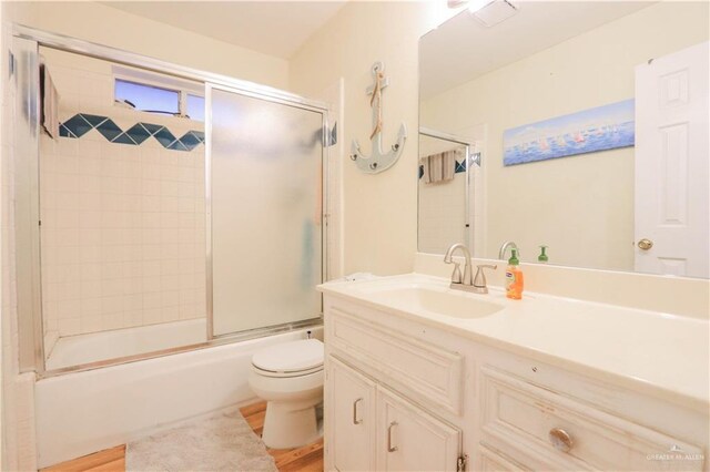 bathroom with enclosed tub / shower combo, toilet, vanity, and wood finished floors