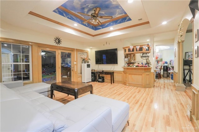 living room featuring a raised ceiling, ornamental molding, a ceiling fan, and light wood finished floors