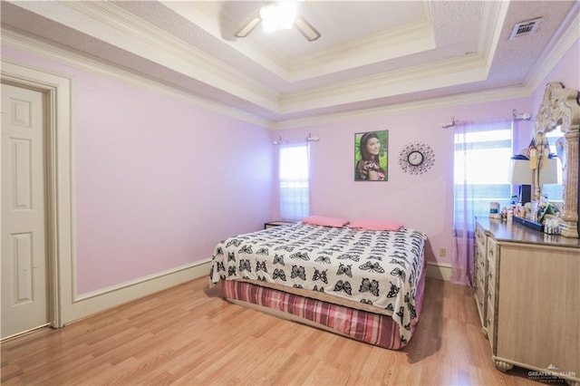 bedroom featuring light wood-style floors, visible vents, a raised ceiling, and multiple windows