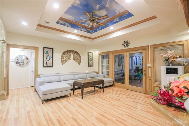 living area with visible vents, a raised ceiling, ornamental molding, and light wood finished floors