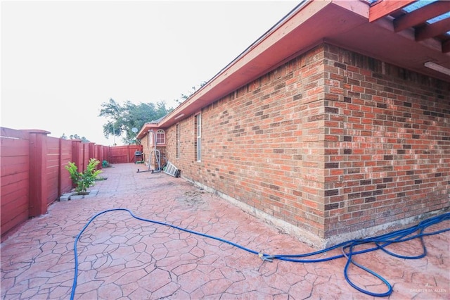 view of side of home with a patio area, brick siding, and a fenced backyard