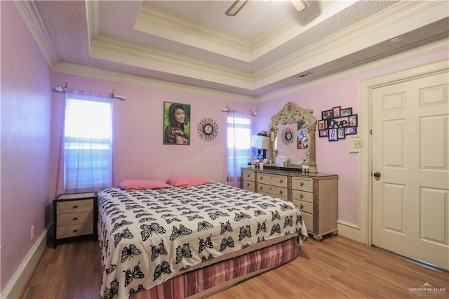 bedroom featuring a raised ceiling, light wood-style floors, and ornamental molding