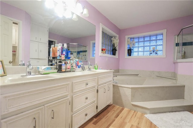 bathroom with double vanity, a stall shower, wood finished floors, a bath, and a sink