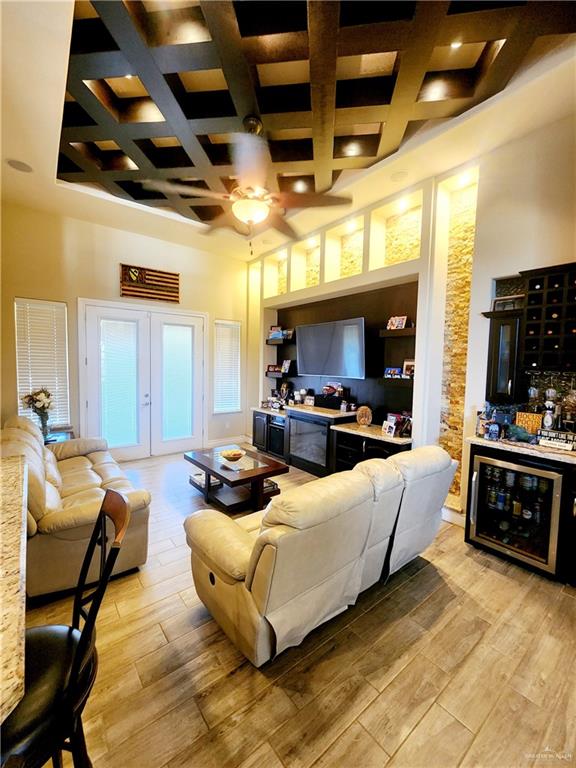 living room featuring a high ceiling, light hardwood / wood-style flooring, ceiling fan, and coffered ceiling