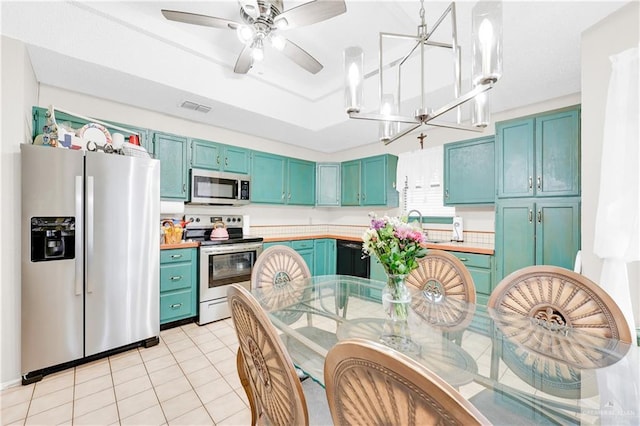 kitchen with blue cabinets, light tile patterned floors, a tray ceiling, stainless steel appliances, and ceiling fan with notable chandelier