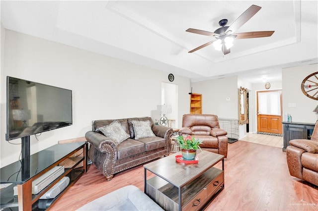 living room featuring a raised ceiling, ceiling fan, and light wood-type flooring