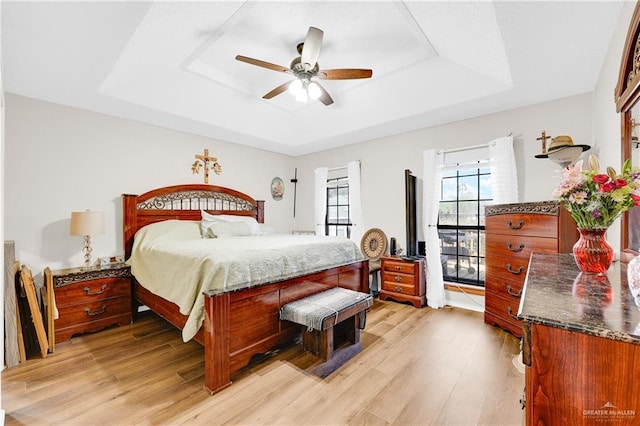 bedroom with ceiling fan, light wood-type flooring, and a tray ceiling