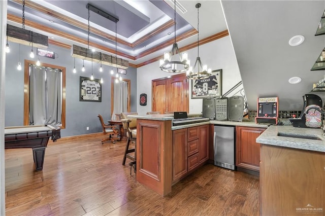 kitchen with a tray ceiling, a sink, a peninsula, fridge, and brown cabinets