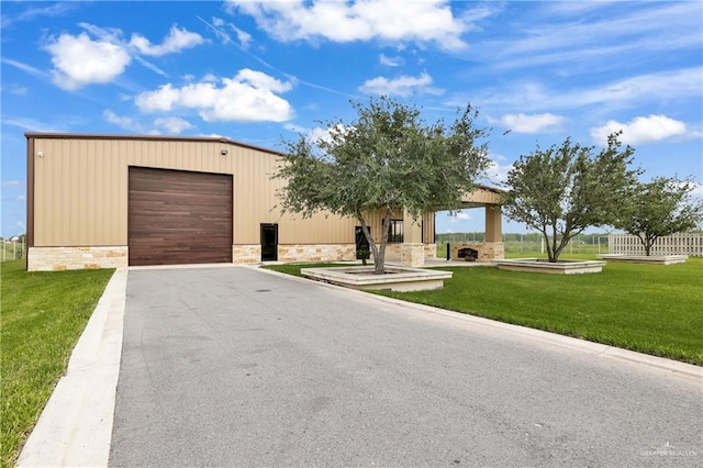 view of front of home featuring stone siding, an outbuilding, a front yard, and aphalt driveway
