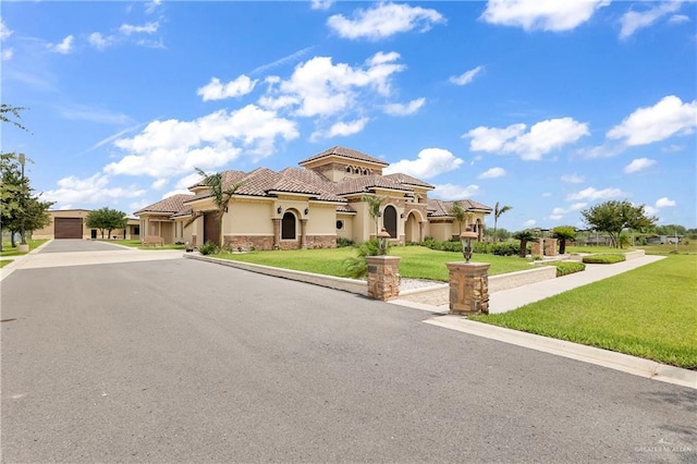 mediterranean / spanish house with stone siding, stucco siding, a front lawn, a tiled roof, and a garage