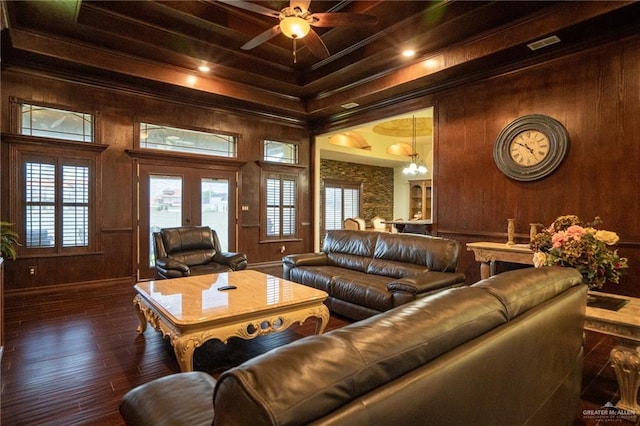 living room with ceiling fan with notable chandelier, wood walls, dark wood-type flooring, and a high ceiling