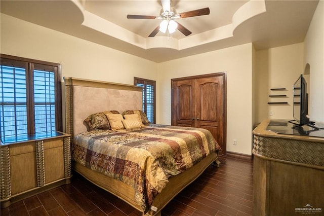 bedroom with ceiling fan, a raised ceiling, and multiple windows