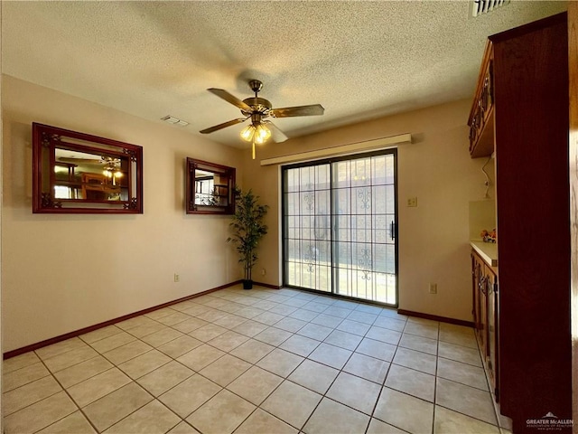 empty room featuring a textured ceiling, ceiling fan, and light tile patterned flooring