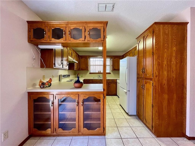 kitchen with a textured ceiling, white fridge, light tile patterned flooring, and stainless steel range with electric stovetop