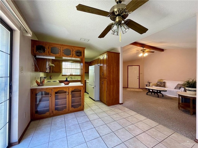 kitchen with ceiling fan, vaulted ceiling with beams, white fridge, a textured ceiling, and light carpet