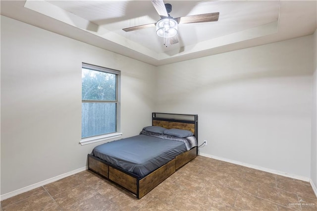 bedroom featuring ceiling fan, a raised ceiling, and baseboards