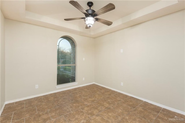 empty room featuring ceiling fan, a tray ceiling, and baseboards