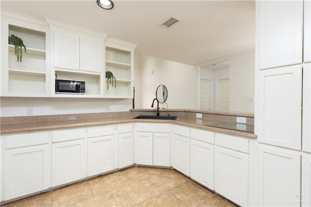 kitchen with black microwave, visible vents, white cabinetry, open shelves, and a sink