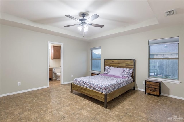 bedroom with ensuite bathroom, ceiling fan, and a tray ceiling