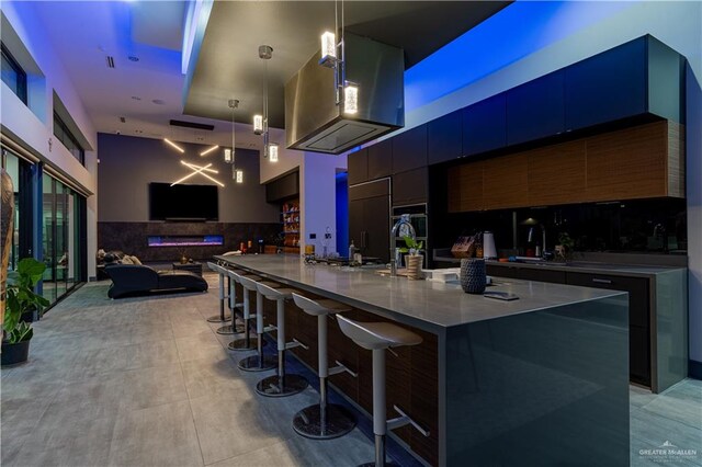 kitchen featuring paneled built in refrigerator, a large island with sink, decorative light fixtures, a breakfast bar area, and range hood