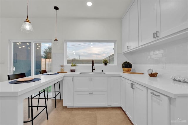 kitchen with a peninsula, a sink, a healthy amount of sunlight, a kitchen breakfast bar, and backsplash