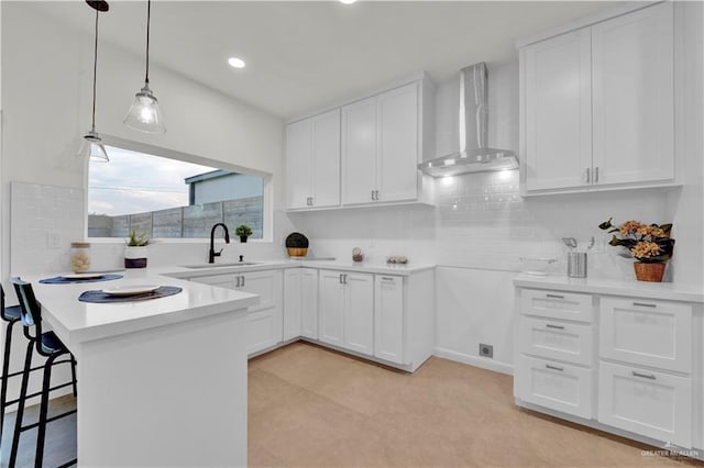 kitchen featuring wall chimney exhaust hood, a breakfast bar area, a peninsula, white cabinetry, and a sink