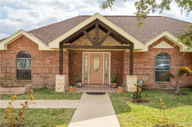 view of front facade with brick siding, a front lawn, and roof with shingles