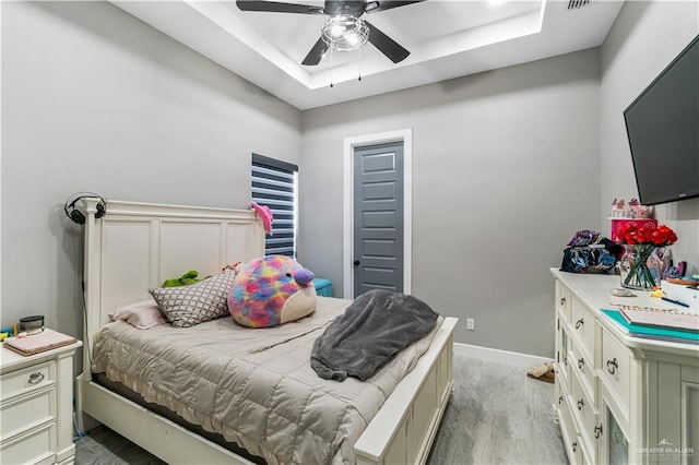 bedroom featuring a raised ceiling, ceiling fan, and light wood-type flooring