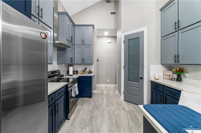 kitchen featuring tasteful backsplash, wall chimney range hood, blue cabinets, and appliances with stainless steel finishes