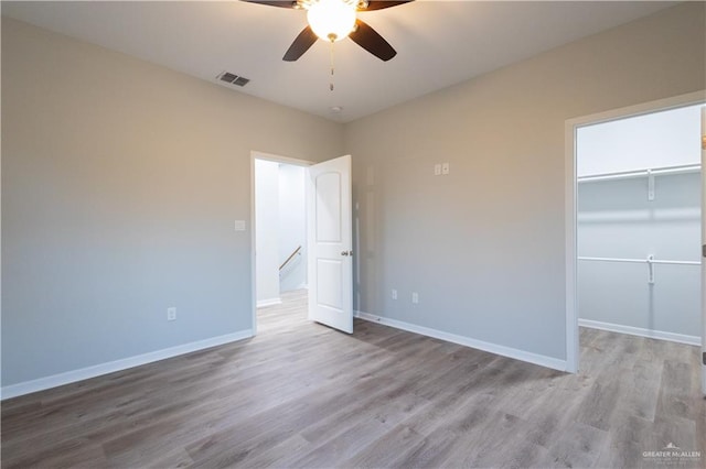 unfurnished bedroom with a closet, a spacious closet, light hardwood / wood-style flooring, and ceiling fan