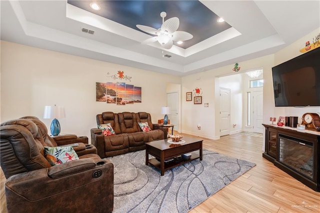 living room featuring a raised ceiling, ceiling fan, and light hardwood / wood-style flooring