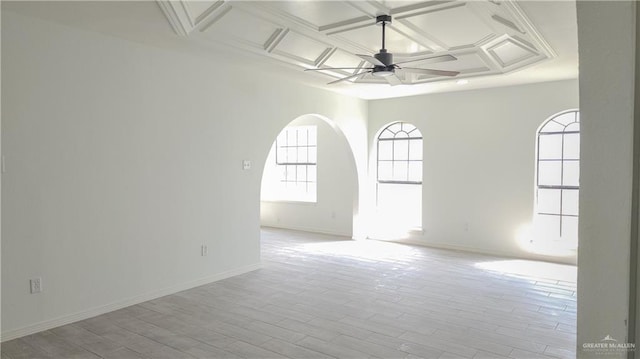 spare room with arched walkways, coffered ceiling, baseboards, ceiling fan, and light wood-style floors