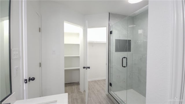 bathroom with a stall shower, a walk in closet, and wood finish floors