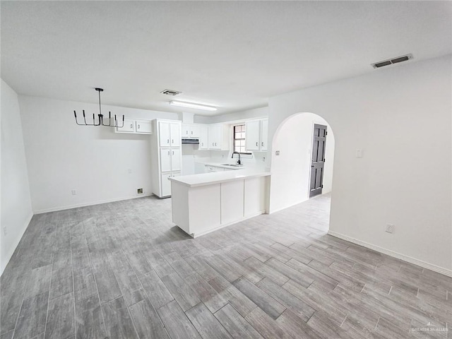 kitchen with arched walkways, a peninsula, a sink, visible vents, and light wood finished floors