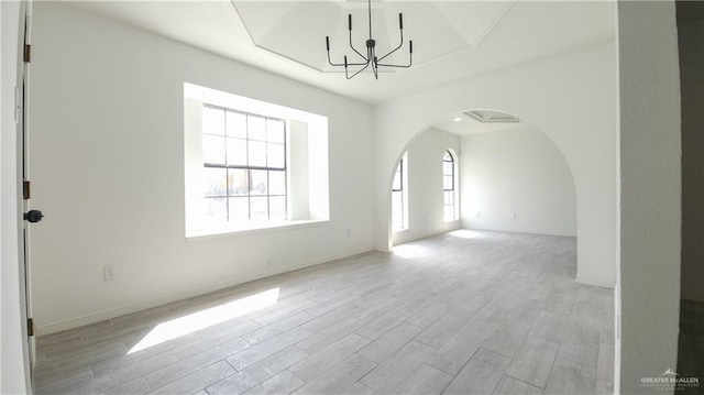 unfurnished room with arched walkways, wood finished floors, baseboards, and an inviting chandelier